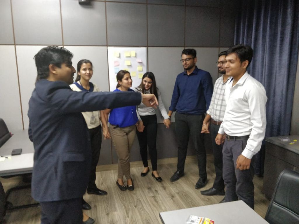 Students standing in a circle holding hands while a facilitator points across the room